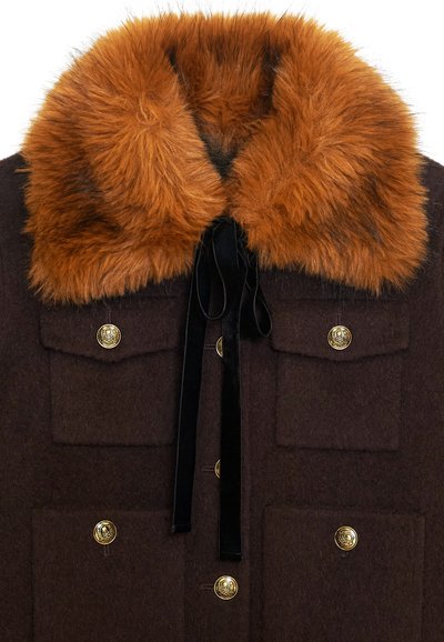 Abrigo de lana marrón con un gran collar de piel de naranja, botones dorados y una cinta de terciopelo negro. Se pueden ver cuatro bolsillos frontales.