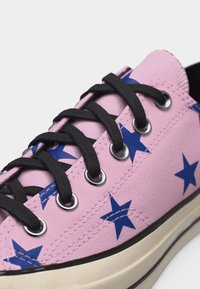 Ροζ πάνινο αθλητικό παπούτσι με μαύρα κορδόνια, μπλε αστέρια, ασημί οπές και υπόλευκη σόλα από λάστιχο με μαύρη περίμετρο.