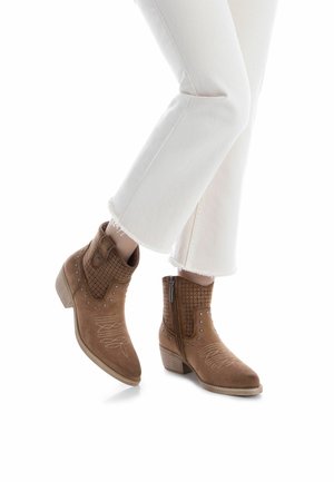 Stivaletti alla caviglia in camoscio marrone con design perforato, borchie argento e dettagli ricamati. Tacco basso impilato e chiusura laterale con cerniera.