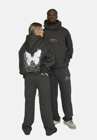 Dunkelgraue Hoodies und Hosen aus weichem Stoff, mit einem weißen Schmetterlingsdesign auf dem Rücken und dezentem Logo-Detail auf der Front.