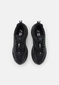 Black athletic sneakers with mesh material, rounded toe, thick rubber sole, and textured accents. Features contrasting gray laces and branding.