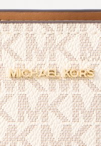 Piele artificială texturată crem prezintă un model repetat cu logo-ul auriu "MICHAEL KORS" expus proeminent în centru.