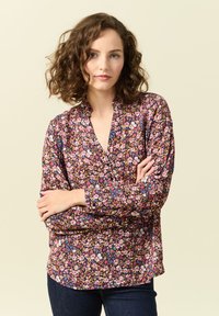 Blommig blus med djup V-urringning, långa ärmar och lös passform. Mönstret har rosa, lila och gula blommor på en mörk bakgrund.