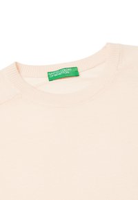 Svetle broskvové svetr s vroubkovaným kulatým výstřihem, měkkou strukturou a detailem šití. Zelená nálepka "United Colors of Benetton" je viditelně vystavena.