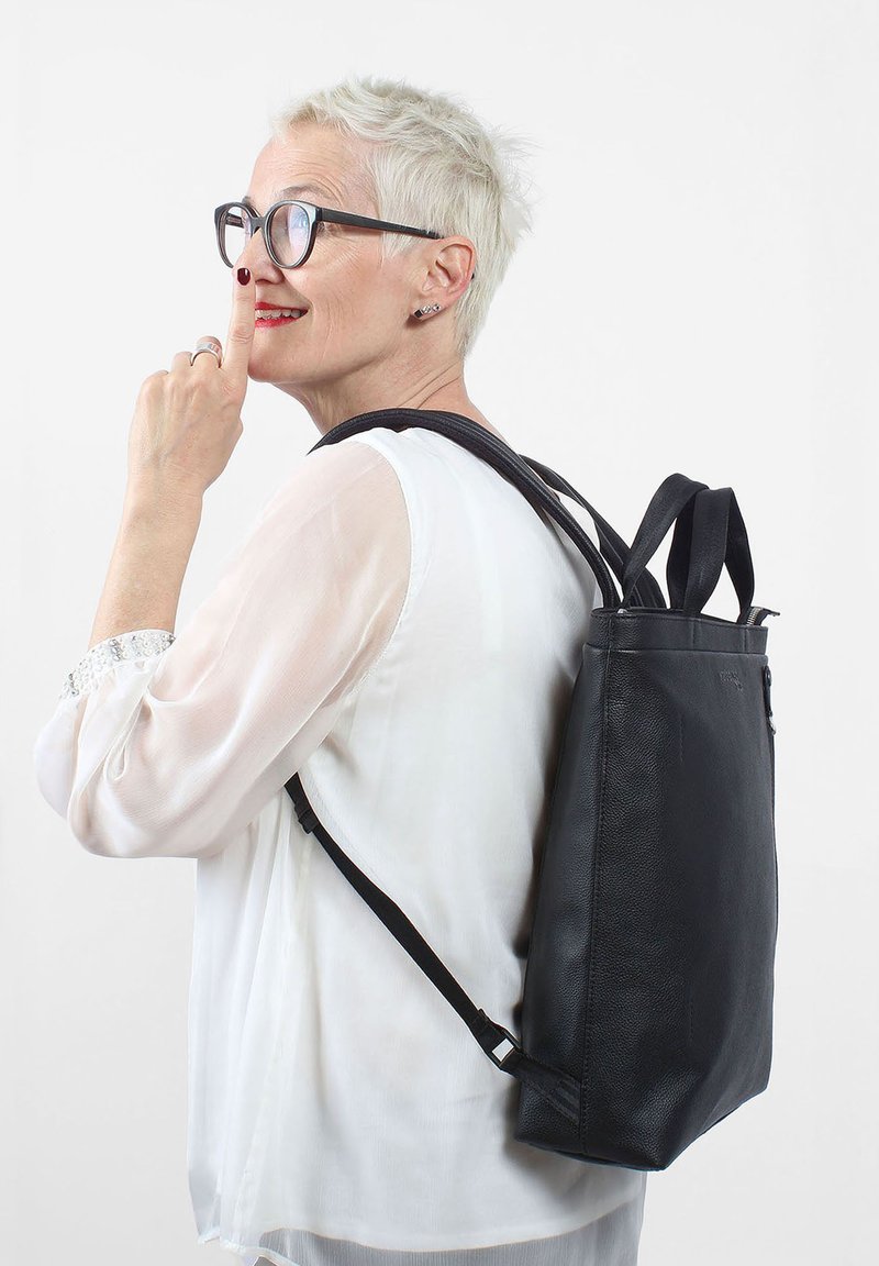 Svart läderryggsäck med en slät textur, rektangulär form, justerbara remmar och dubbla topphandtag. Har en dragkedjestängning.