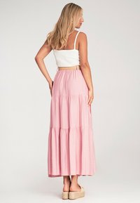 Helle rosa, gestufte Maxi-Rock aus weichem Stoff, kombiniert mit einem weißen, figurbetonten Oberteil. Verfügt über einen verstellbaren Bund und lässige Sandalen.