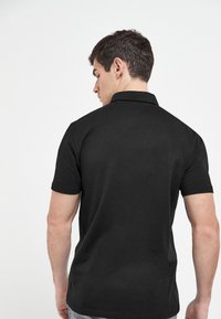 Schwarzes Polohemd mit kurzen, figurbetonten Ärmeln, aus einem glatten Stoff gefertigt. Verfügt über einen klassischen Kragen und eine dezente Textur.