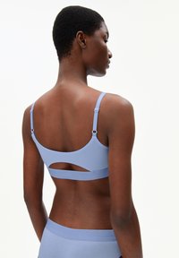 Soutien-gorge bleu clair avec des bretelles réglables, en tissu texturé et un détail découpé à l'arrière. Design lisse et sans couture, ceinture bleue assortie visible.