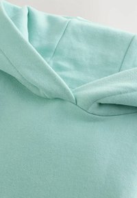 Gai mentolzaļš hoody ar teksturētu audumu, piedāvājot mīkstu, atvieglinātu kakla izgriezumu un saskatāmu dūrienu gar šuvēm.