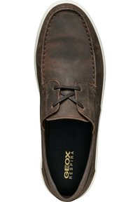 Zapato de cuero marrón con superficie texturada, con suela blanca, interior negro y cordones marrones a través de ojetes. Logotipo de la marca visible en el interior.