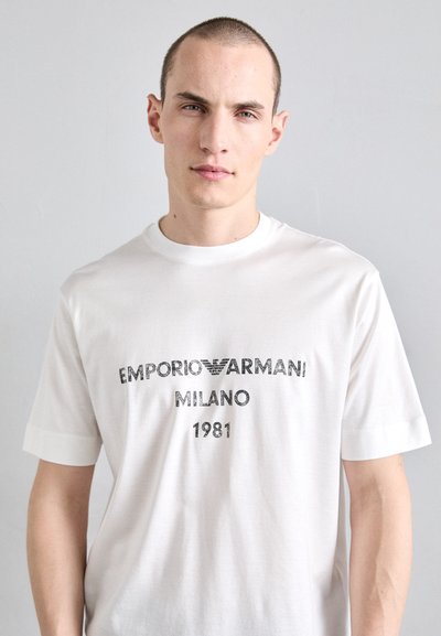 T-shirt en coton blanc avec texte imprimé "EMPORIO ARMANI MILANO 1981" en noir avec un accent logo, col rond et manches courtes.