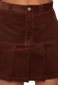 Brun kordflod mini kjol med vertikal ribbad textur, med en plisserad design och metallknäppning i midjan.