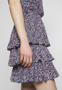 Jupe à volants à étages avec des couches de volants, en tissu léger bleu marine orné de petites fleurs multicolores. Taille texturée.