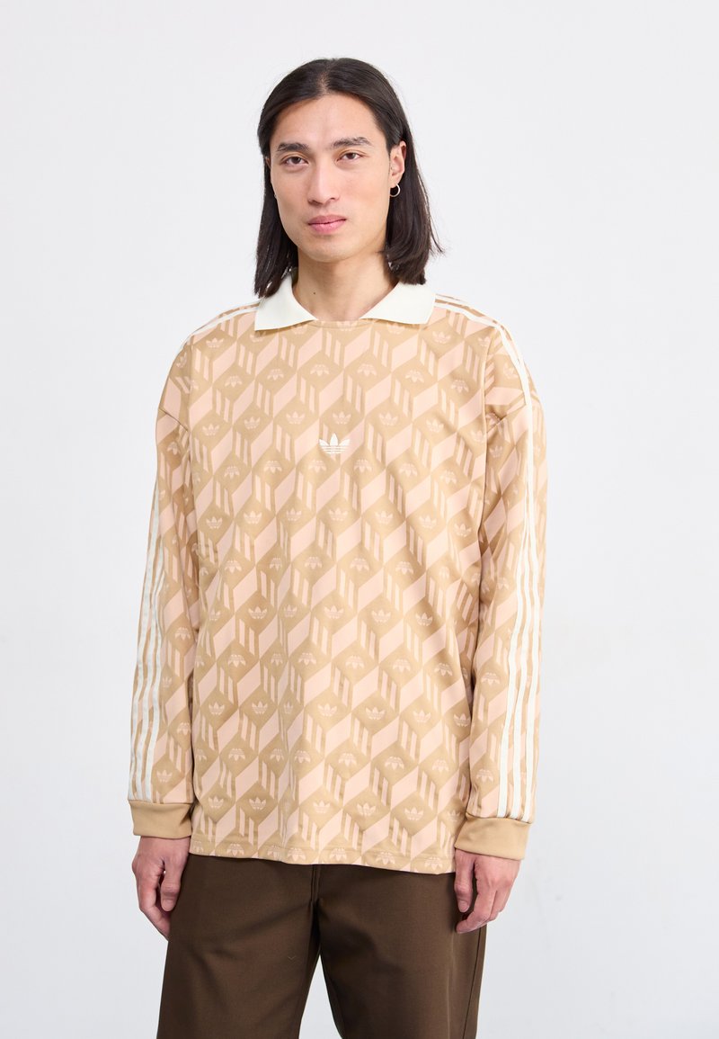 Long-sleeve beige shirt with geometric pattern, white collar, and three white stripes along the sleeves. Adidas logo on the front.