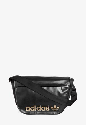 Černá messenger taška z umělé kůže s dlouhým popruhem, zdobená zlatým logem "adidas" a designem trojlístku, se zipovou kapsou a hladkým povrchem.