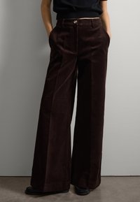 Bruine corduroy wijde broek met hoge taille, voorzien van voorzakken en een enkele knoopsluiting. Gladde textuur met verticale ribbel.