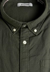 Tumedat rohelised nööbitavad särk, millel on laia kaeluse, valged nööbid, tekstuuriga kangas ja rinna tasku. Brändi silt: JACK & JONES.