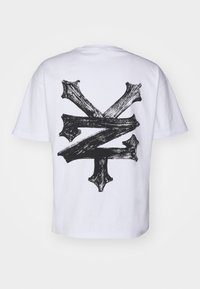 Hvid bomulds t-shirt med et stort sort grafisk design på ryggen, der ligner krydsende penselstræk og skarpe kanter.