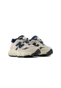 Ζευγάρι μπεζ και ναυτικού μπλε παπούτσια New Balance με χοντρές σόλες και επάνω μέρος από δίχτυ και σουέντ σε λευκό φόντο.