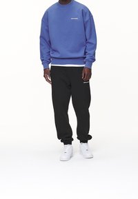 Felpa viola con collo rotondo e polsini a coste, abbinata a pantaloni felpa neri con accenti del logo bianco, completata da sneakers bianche.