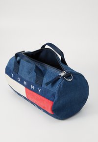 Sac de voyage en denim bleu avec des accents rouges et blancs, doté d'une fermeture éclair, de poignées robustes et de texte imprimé sur le côté.