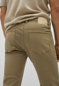 Pantalons en coton beige avec une coupe ajustée, dotés d'une taille droite, de deux poches arrière et d'un patch en cuir de la marque sur la taille.