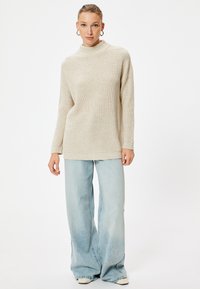 Cremfarbener Strickpullover mit hohem Kragen, kombiniert mit hellblauen, weit geschnittenen Jeans. Weiche Textur und lockere Passform für maximalen Komfort.