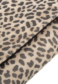 Tessuto a fantasia leopardata in tonalità di beige e nero, con cuciture visibili e una superficie liscia.