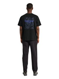Homme debout, de dos, portant un T-shirt noir avec l'inscription bleue "OFF DUTY GEAR" et un motif abstrait dans le dos, pantalon noir, chaussures grises.