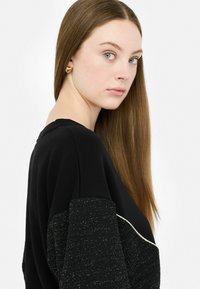 Zwarte top met een getextureerde schouder met gouden accenten, met een elegante silhouet. Het gladde zwarte stof contrasteert met de glanzende metallic details.