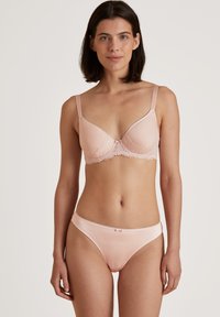 Beugel BH en bijpassende bikini in lichtroze. Kenmerkt zich door kantdetails langs de bovenrand en een decoratieve strik in het midden. Glad aanvoelend.