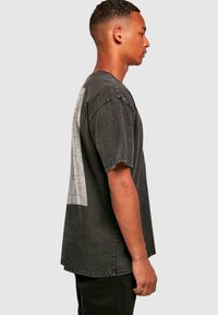 Sort T-shirt med korte ærmer og et puslespilsdesign på bagsiden, lavet af bomuldsdenimstof, med en afslappet pasform og rå kant.