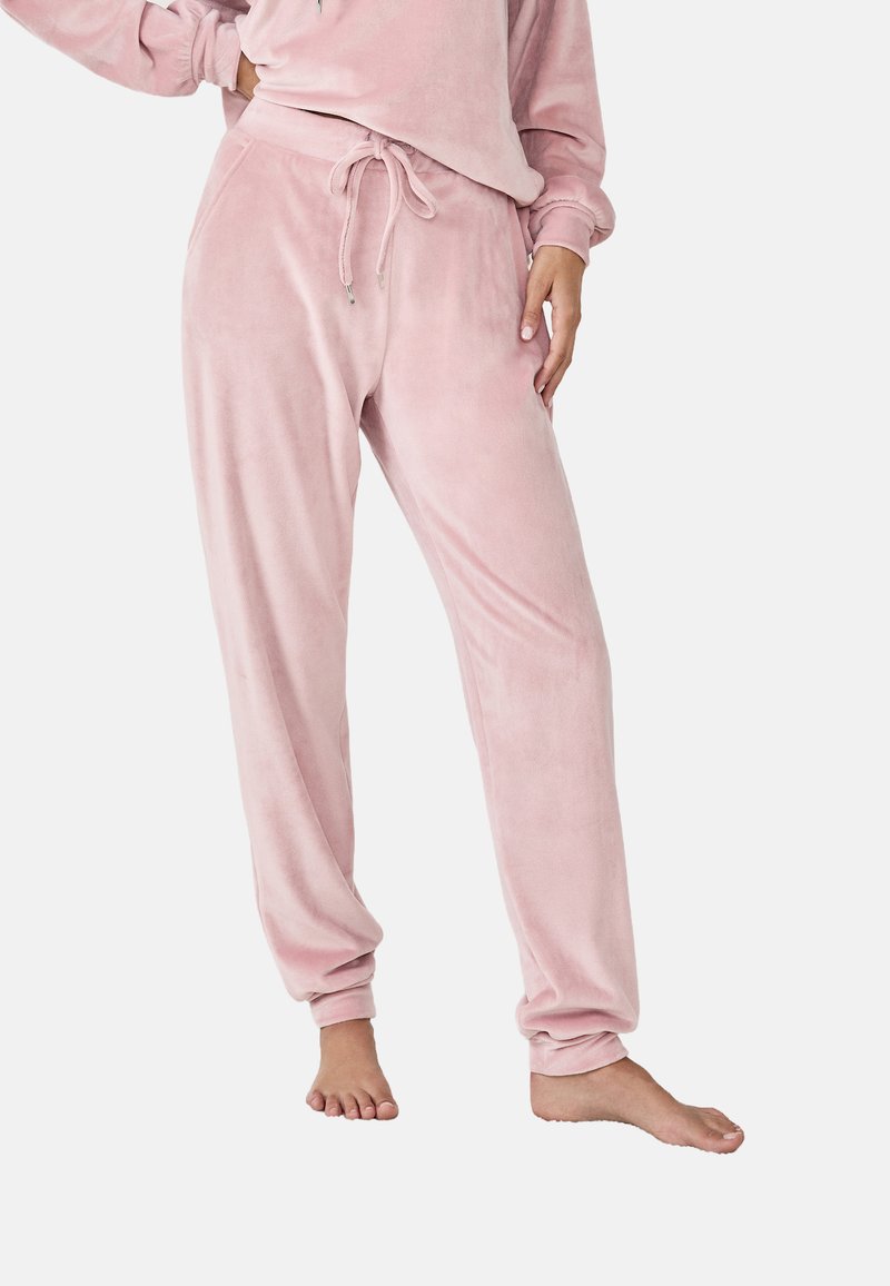 Pantalon de jogging en polaire rose avec une taille élastique à cordon, des poches latérales inclinées et une coupe décontractée qui se resserre aux chevilles. Texture douce sur l'ensemble.