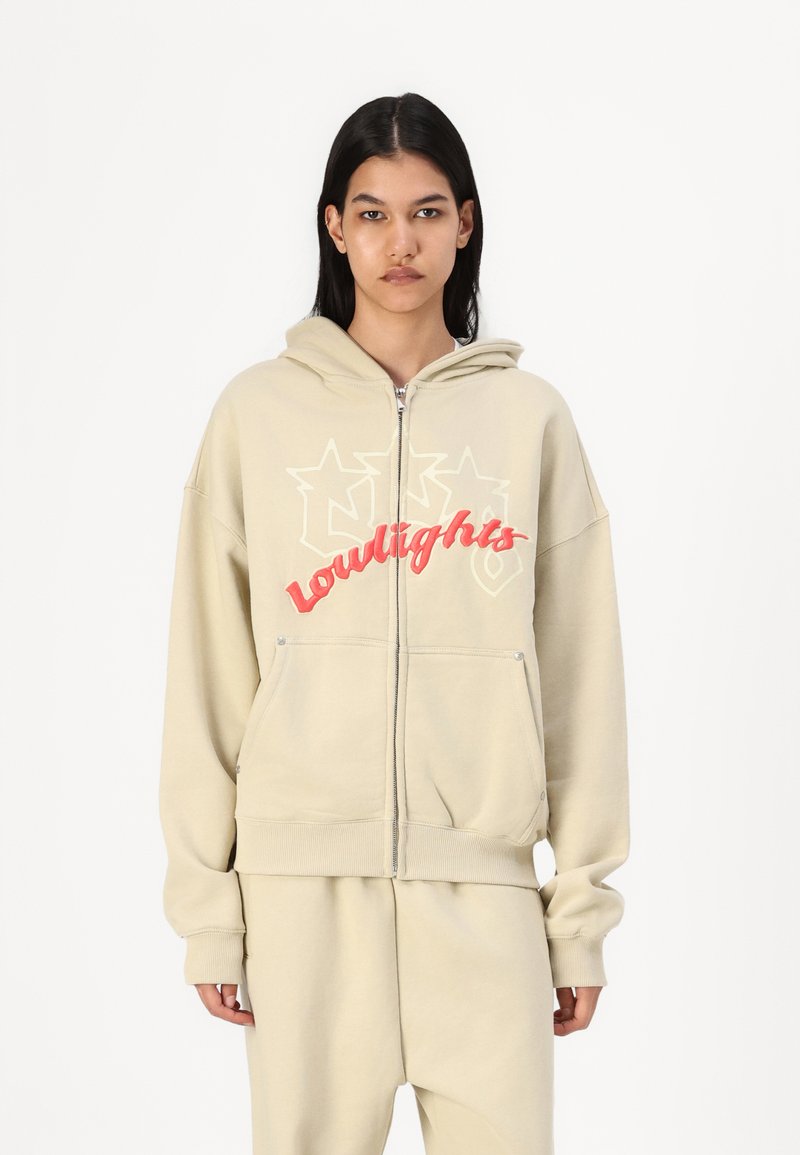 Beige zip-up hoodie with a large red and white "lowlights" graphic, featuring a front pocket and soft, textured fabric.
