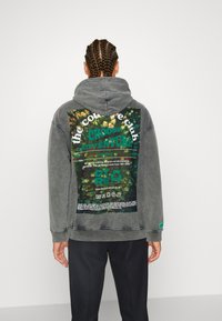 Sudadera gris con una gran gráfica colorida en la parte posterior que incluye el texto "the couture club" y "CHOOSE ADVENTURE". Material de algodón.