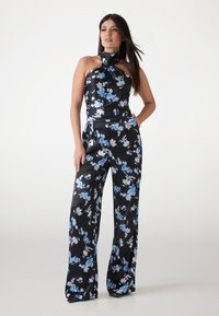 Salopetă neagră cu flori, cu guler halter și detaliu legat, flori mari albastre și albe și pantaloni largi dintr-un material neted.