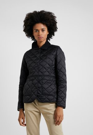Black quilted jacket with a collar, featuring a fitted design and snap buttons, paired with light khaki trousers. Smooth texture.