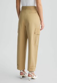 Pantalons cargo kaki avec une coupe décontractée, des poches avant et arrière, des chevilles à revers et une texture lisse. Accentué d'un petit logo à l'arrière.