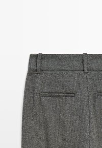 Pantaloni in lana grigia con texture, dotati di passanti per cintura e due tasche posteriori orizzontali su uno sfondo bianco.