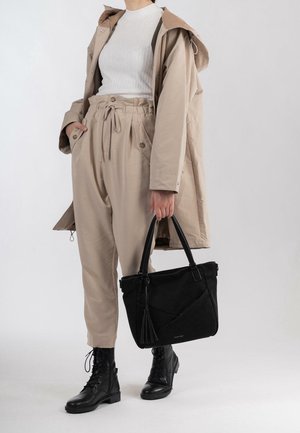 Svart tote-väska med texturerad yta, med dragkedjestängning och tofsdetalj. Bärs med en beige outfit och svarta snörstövlar.