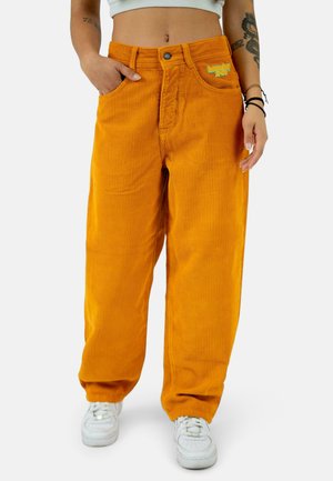 Orange corduroy wide-leg pants with front pockets, a button closure, and embroidered branding on the left pocket. Worn with white sneakers.