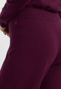Burgunderfarbene Strickhosen mit figurbetonter Passform. Mit einem roten 'X'-Akzent am Bund. Weicher Stoff und elastisches Material für Komfort.