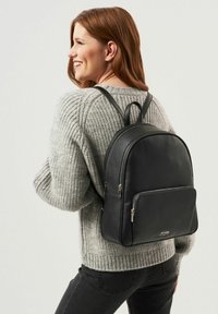 Czarny skórzany plecak o gładkiej teksturze, z podwójnymi zamkami błyskawicznymi, oraz przednią kieszenią. Regulowane paski i zaokrąglony design u góry.