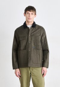 Quilted olivgrüne Jacke mit einem schwarzen Cordkragen, ausgestattet mit zwei Fronttaschen und Druckknöpfen, aus einem synthetischen Material hergestellt.