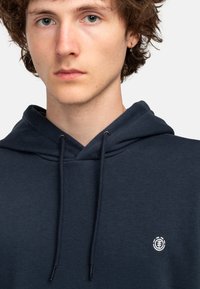 Marineblauwe pullover hoodie met een trekkoord, gemaakt van een katoenmix, met een klein geborduurd logo op de linkerborst.
