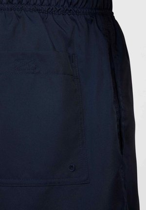 Marinblå shorts i lätt tyg, med elastisk midja, sidofickor och ett dekorativt sytt mönster på fickan.