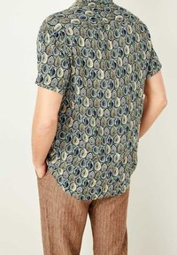 Kurze Ärmel Hemd mit grünem Hintergrund und einem sich wiederholenden Muster aus ovalen Formen in Marineblau, Creme und Schwarz. Mit einem spitzen Kragen.