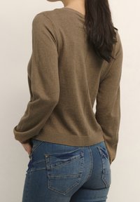 Pull en tricot marron à manches longues et à ourlet côtelé, associé à un jean en denim bleu avec des coutures décoratives sur les poches arrière.