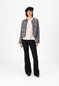Grå tweedjakke med svart innfatning og knapper, beige genser, svarte vide bukser og svart beret. Glatt tekstur, skreddersydd design.