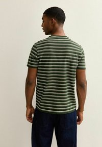 Camiseta de manga corta a rayas verdes y blancas con cuello redondo, hecha de un tejido suave, combinada con pantalones azul oscuro, vista por la parte de atrás.